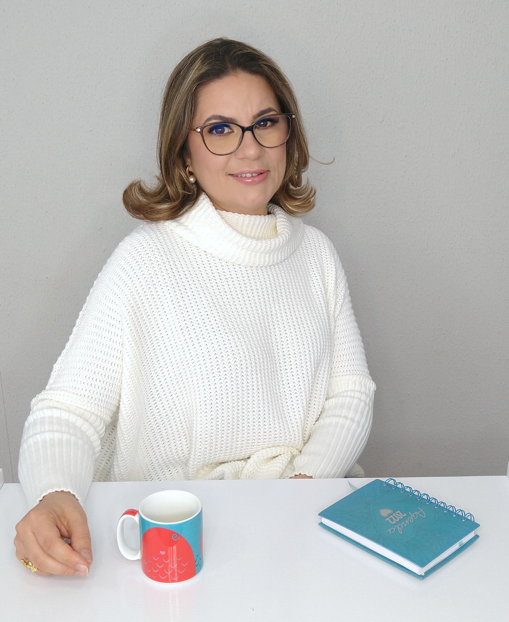 Bárbara Senna sentada à mesa com uma caneca e um caderno